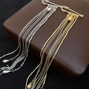 Elegant gold and silver safety pin brooches with long water drop tassels on jewelry box.