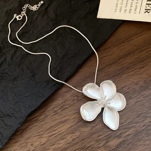 Detail view of the matte silver flower pendant necklace on a vintage wood surface
