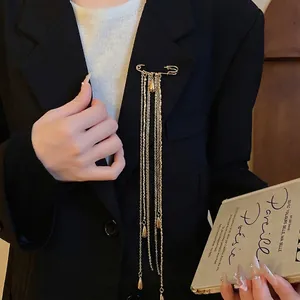 Elegant gold safety pin brooch with long tassel chains and waterdrop charms on a blazer.