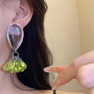 Close-up detail of a resin teardrop earring with green bead tassels worn on an ear