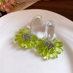 Close-up of green resin teardrop tassel earrings with silver needles on a white plate.