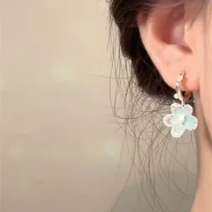 Close-up of minimalist light blue flower earring with pearl detail on ear.