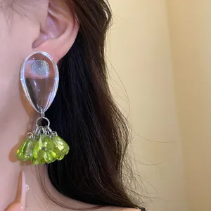 Close-up detail of silver needle resin teardrop earrings with green bead tassels