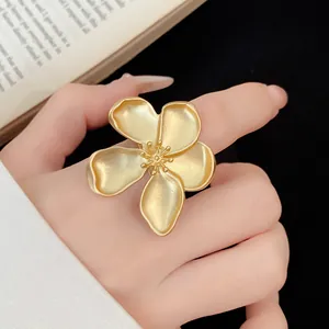 Detailed close-up of vintage style matte gold five-petal flower ring worn on a finger