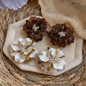 Elegant acetate flower earrings with glass beaded center on woven mat background