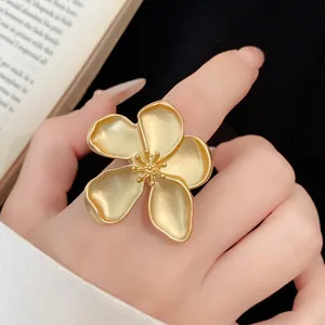 Exquisite close-up of large matte gold flower ring on finger against vintage book page