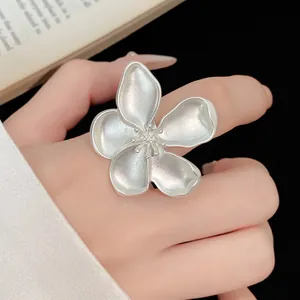 Macro detail of a matte silver flower ring with intricate petal texture on hand