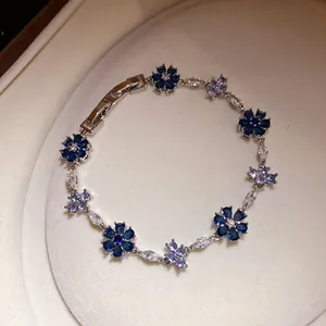 Detailopname van een zilverkleurige armband met blauwe en heldere zirkoonbloemen