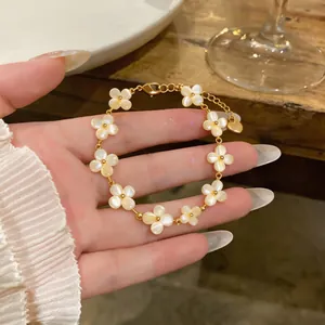 Gros plan d'un bracelet en or avec des breloques fleurs en œil de chat dans la main