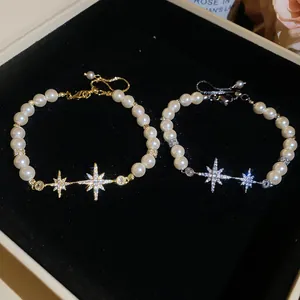 Detail view of two elegant 18k gold plated star charm pearl bracelets on black velvet