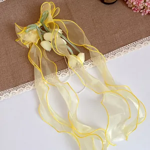 Dettaglio clip per capelli fiocco mughetto giallo con eleganti nastri lunghi.