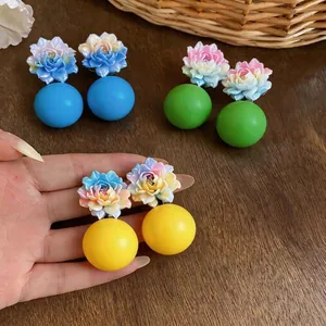 Vibrant resin lotus flower earrings with large colorful ball drops on wooden background.