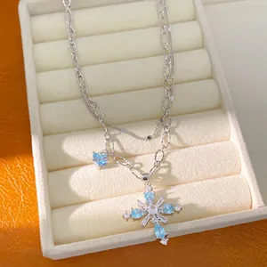 Detail of a double-layered silver necklace featuring a sparkling blue zircon cross pendant
