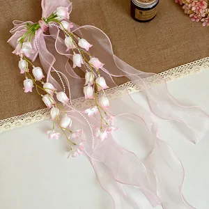 Vista dettagliata del delicato fiocco in organza rosa e del fermaglio per capelli mughetto.