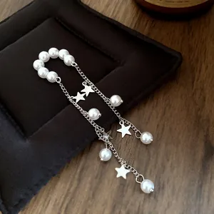 Close-up of minimalist pearl and star tassel ear cuff with silver chains and beads.