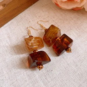 Macro detail of Maillard style vintage amber acrylic geometric drop earrings on linen