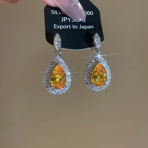 Macro view of luxurious yellow pear-cut zircon teardrop earrings with shimmering halo detail