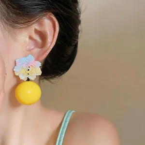 Macro view of a colorful resin flower earring with a large yellow bead pendant on a model.