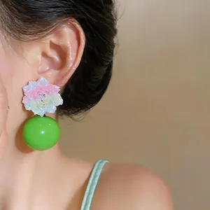 Detail view of colorful resin flower earring with a large glossy green spherical drop.