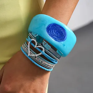 Macro view of blue resin bangle and multi-layer leather bracelets with silver heart on wrist