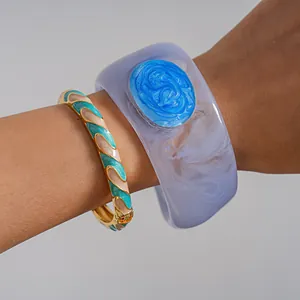 Detail shot of wide blue marbled resin bangle and teal wavy enamel gold bracelet