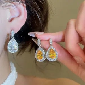Close-up of luxurious teardrop zircon earrings with halo design on model ear.