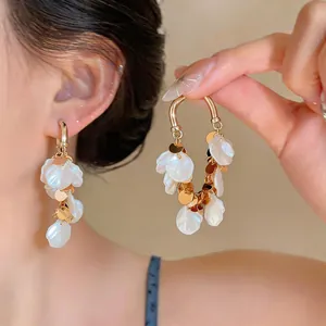 Detail view of French style gold hoop earrings with white petal tassels and gold discs.