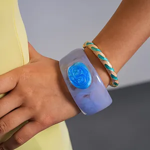 Detailed close-up of a chunky purple resin bangle and colorful enamel twisted bracelet on a wrist
