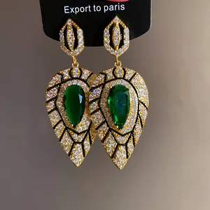 Detailansicht goldener Tropfenohrringe mit smaragdgrünen Steinen und Zirkon-Pavé-Besatz