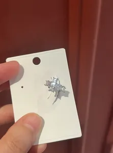 Detailed macro view of a silver-toned cross-shaped zircon ear cuff on a white jewelry card