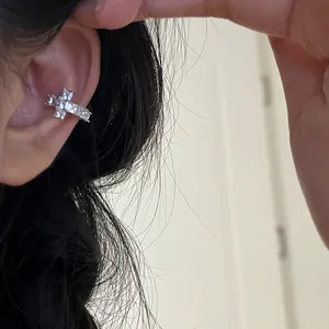 Detailed shot of a silver cross ear cuff with shiny zircons worn on the ear