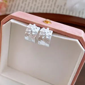 Primo piano di eleganti orecchini a fiore color argento a forma di C su una scatola rosa