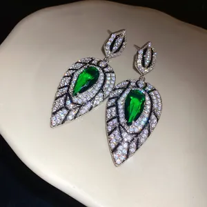 Detailansicht von Tropfenohrringen mit grünen Zirkonia und Kristallen auf Keramik