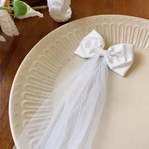 Elegant white fabric bow hair clip with long mesh veil on a decorative plate