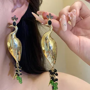 Close-up view of vintage style golden peacock drop earrings with green and black bead fringe