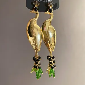 Detailed view of gold peacock earrings with black and green beaded tassels