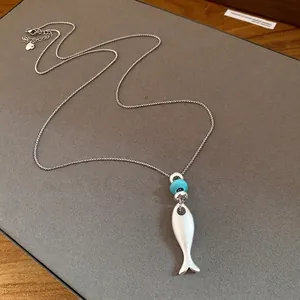 Matte silver fish pendant necklace with turquoise bead on grey background