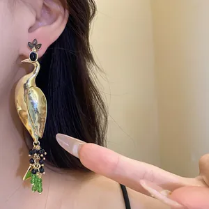 Detailed view of an exaggerated golden peacock pendant earring with black and green beads.