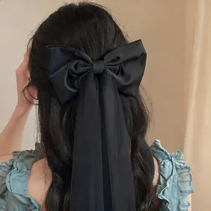 Detail view of a large black fabric bow hair clip with long mesh tassels on hair