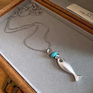 Elegant matte silver fish pendant necklace with a blue stone bead on grey velvet