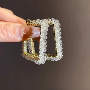 Close-up of elegant square gold-tone hoop earrings wrapped with clear faceted glass beads.