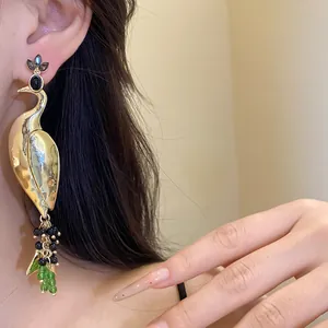 Detail view of an elegant gold peacock dangle earring with colorful beads on a model.