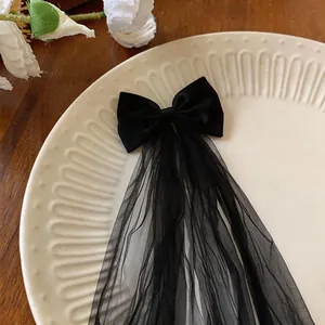 Close-up of black fabric bow hair clip with elegant long mesh tassel on white plate