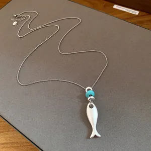 Detailed macro view of matte silver fish pendant necklace featuring a turquoise bead