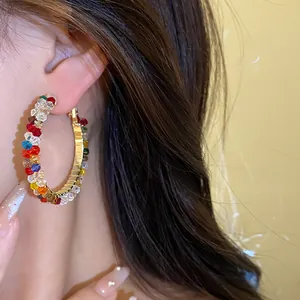 Exquisite close-up of a colorful glass bead hoop earring with a golden metal frame.