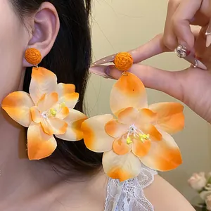 Close-up detail of large orange fabric flower drop earrings worn by an elegant model.