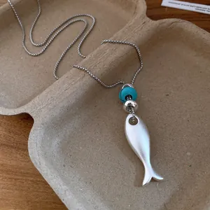 Detailed view of matte silver fish pendant with turquoise bead on a long chain