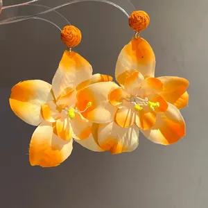Close-up of orange fabric flower earrings with woven raffia studs for beach vacations.