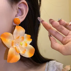 Close-up of large orange fabric flower earring with raffia stud on ear for vacation style.