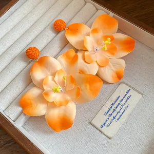 Detailed view of orange raffia fabric flower earrings inside a cream jewelry tray.